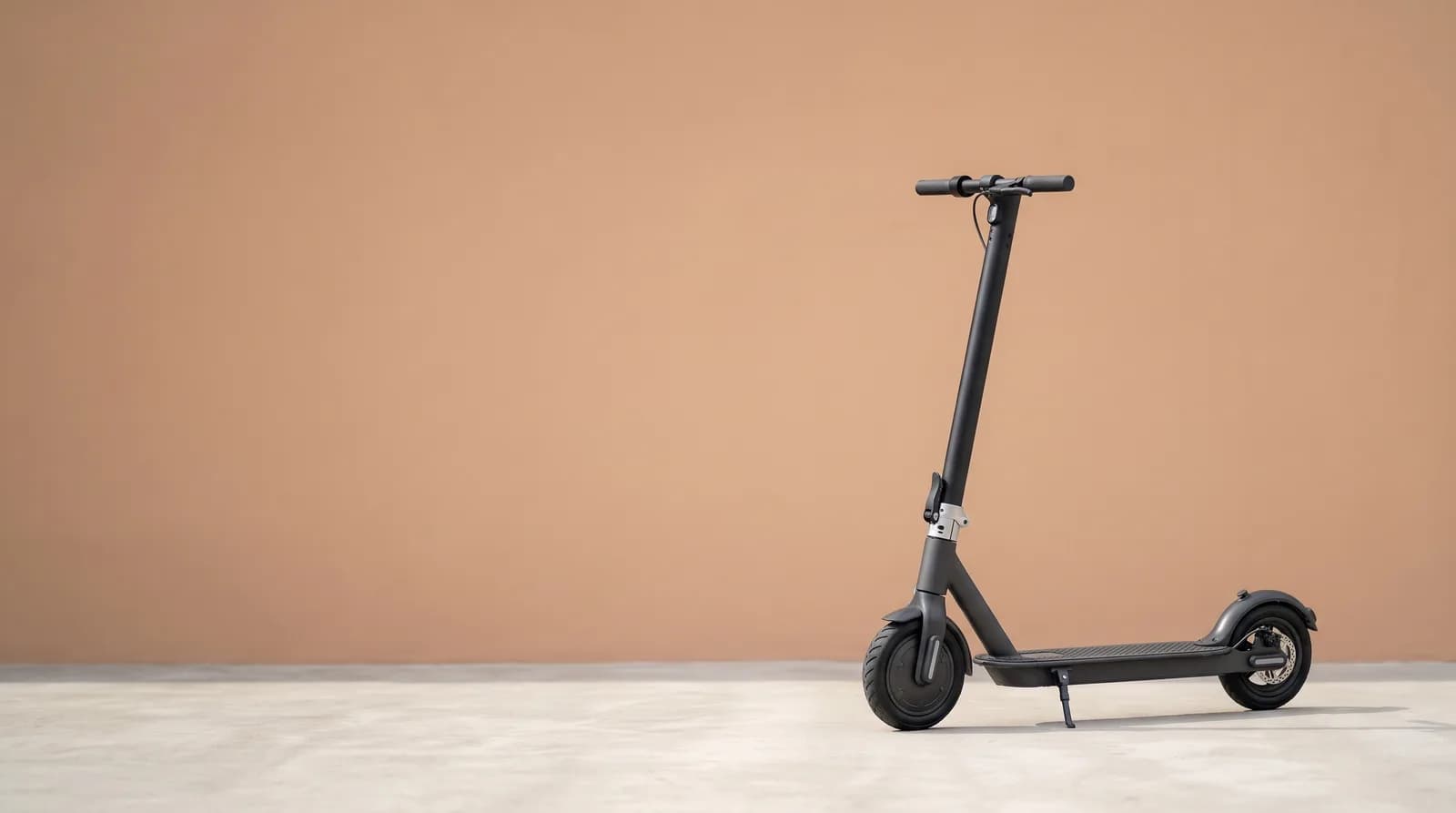 E-Scooter-Akku-Reparatur: schwarzer Elektro-Tretroller vor sandfarbener Wand